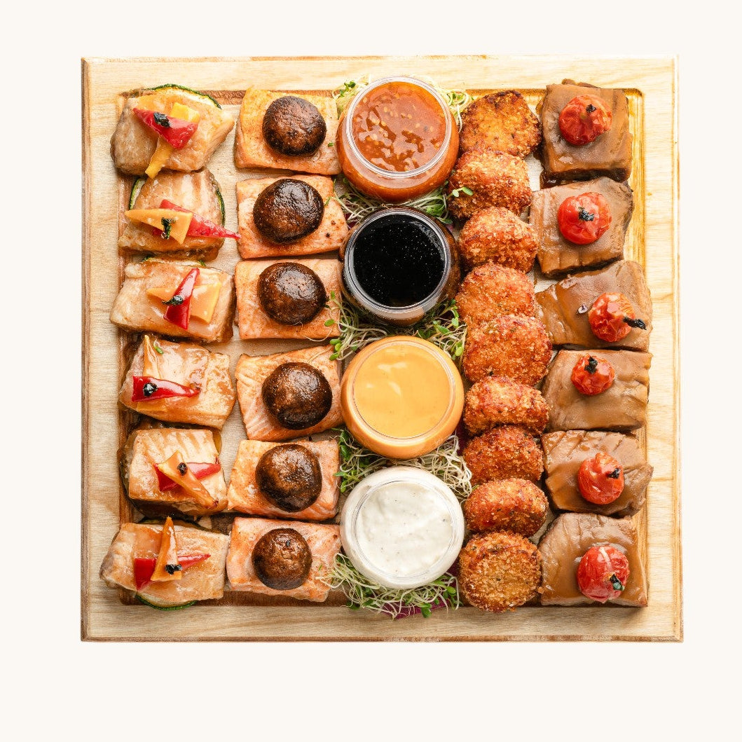 Assorted small bites on a wooden board with dipping sauces.